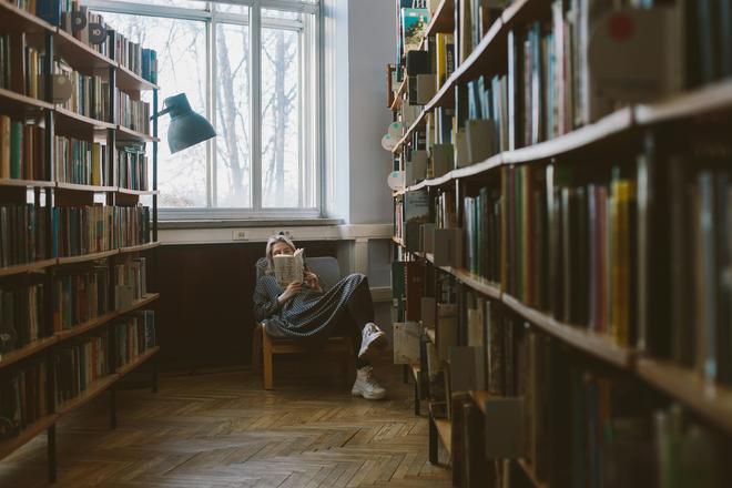 Дівчина читає книгу в бібліотеці