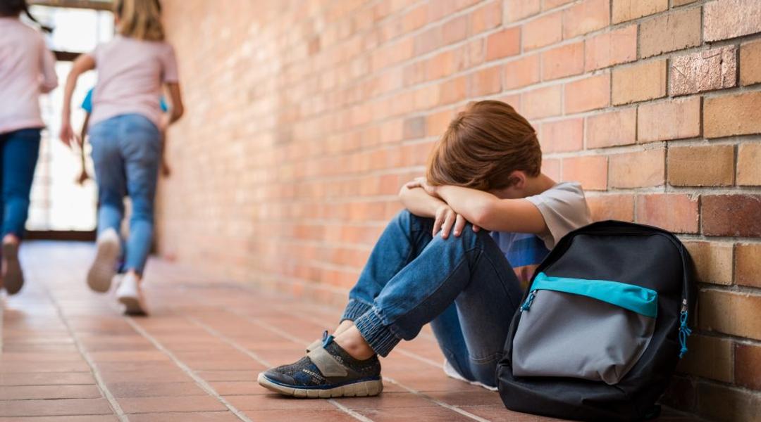 Little boy sitting alone on floor after suffering an act of bullying