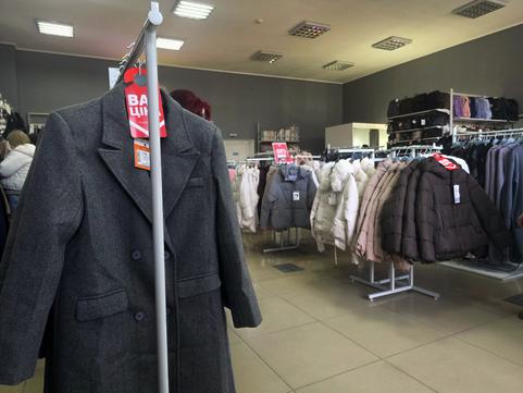 Зала магазину SELLI у Сумах: сіре пальто з биркою «Вау ціна» на передньому плані, стійки з пуховиками, полиці з сумками