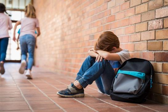 Little boy sitting alone on floor after suffering an act of bullying