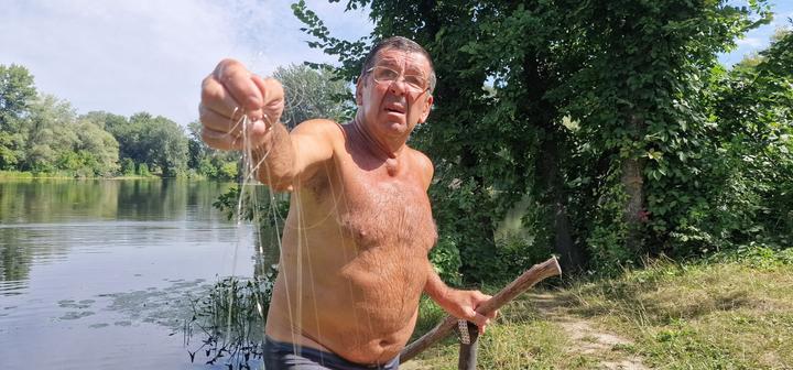 чоловік на березі річки показує у камеру оптоволокно від російського дрону