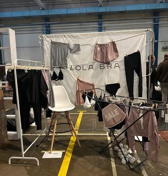 чі Lola Bra на мотузках: білизна, шорти, лосини й футболки, поруч вішак з чорним одягом і сушарка з табличкою SALE